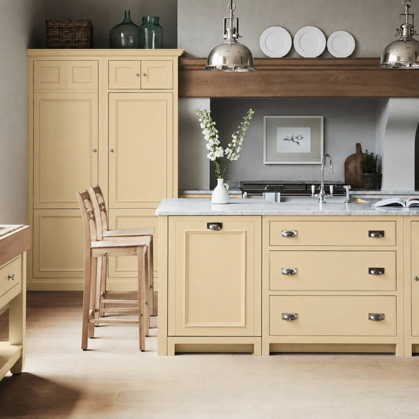 Chichester kitchen with cabinetry painted in Polenta butter yellow, featuring a central island and oak bar stools.