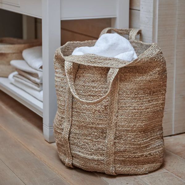 Woven natural-fibre storage basket with a white towel inside, placed next to bathroom washstand.