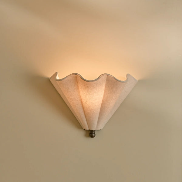 Athena linen scalloped wall light with bronze accents on beige wall, lights on