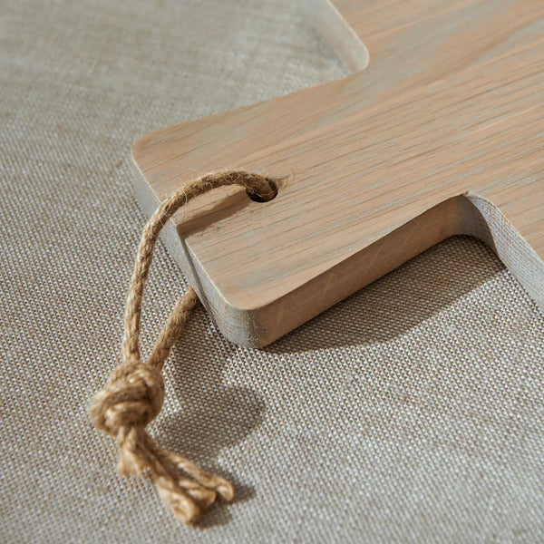 Close up of oak cutting board handle with jute string loop on a neutral linen surface