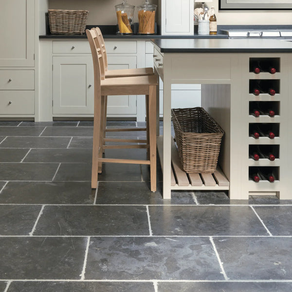 A modern kitchen interior with dark slate tile flooring, white cabinetry, a light wood bar stool, a wicker basket, and a built-in wine rack on the island.