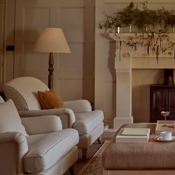Chalford darkened oak floor lamp in upscale living room with beige armchairs and footstool, fireplace, woven rug and cream paneled walls