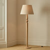 Chalford natural oak floor lamp with linen shade in a carpeted room with beige walls, lights on