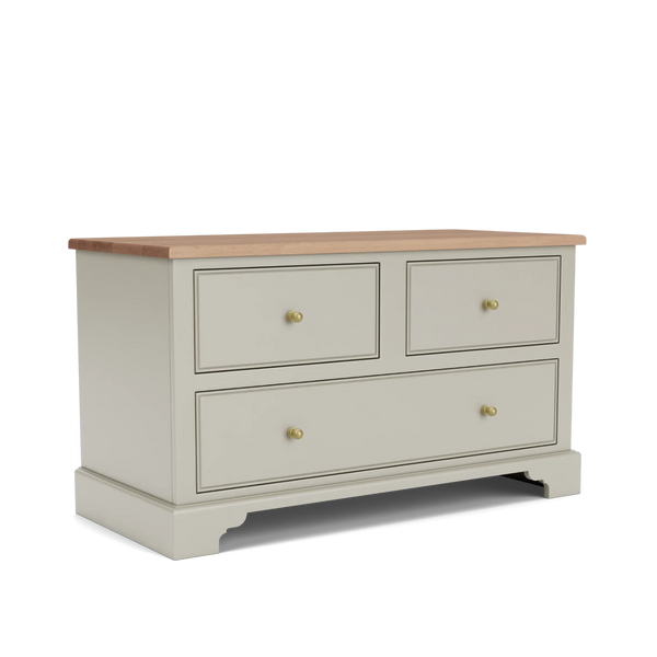 A three-drawer chest of drawers in a warm light gray finish with a natural wood top and small brass knobs, shown on a clean white background.