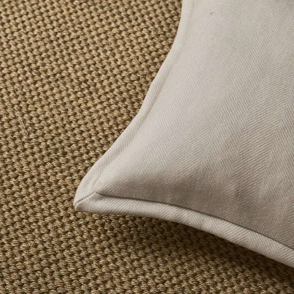 Close-up of a light beige fabric cushion corner resting on a textured brown woven rug.