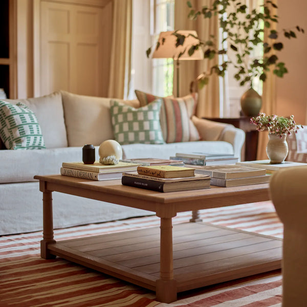 A light natural wood coffee table with a lower shelf, styled with books and small decorative objects in a cozy living room setting.