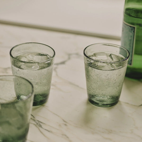 Small translucent green drinking glasses with a speckled, textured finish, arranged on a marble counter.