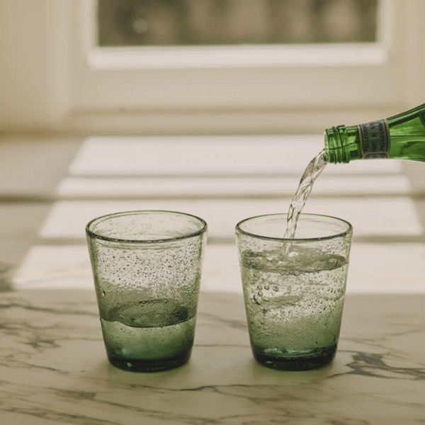 Small translucent green drinking glasses with a speckled, textured finish, arranged on a marble counter.