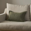 An olive green textured lumbar pillow resting on a light beige upholstered armchair against a neutral gray wall.