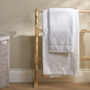 A set of white towels, including a larger bath towel and a smaller hand towel, draped over a light wood ladder rack in a bathroom setting.