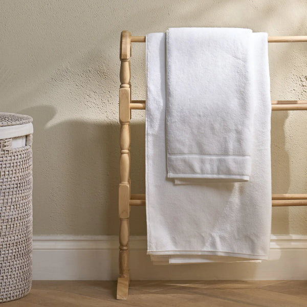 A set of white towels, including a larger bath towel and a smaller hand towel, draped over a light wood ladder rack in a bathroom setting.