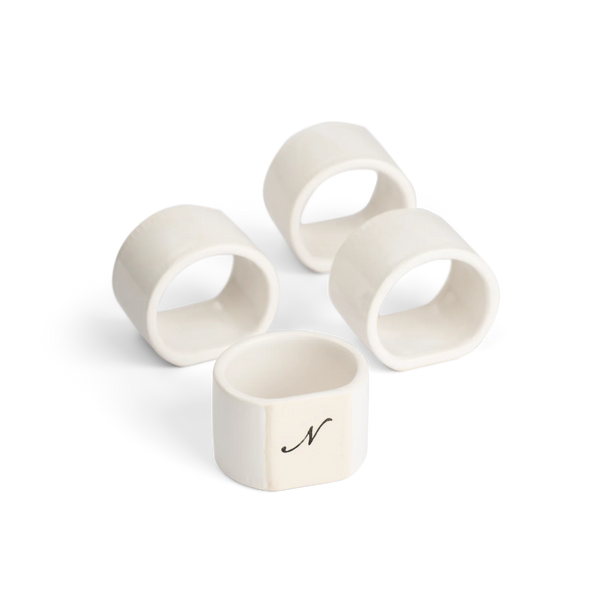 Four off-white ceramic napkin rings on a clean white background, with one ring featuring a black script letter 'N' monogram.
