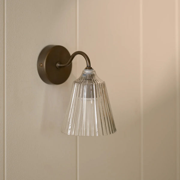 Lennox wall light with brushed bronze base and glass shade on wall.