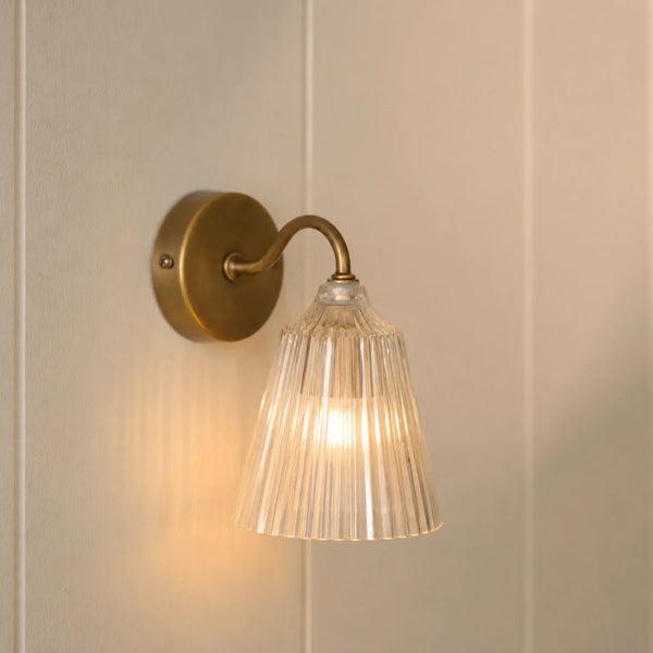 Lennox wall light with brushed brass base and glass shade on wall, light on