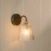 Lennox wall light with brushed bronze base and glass shade on wall, light on
