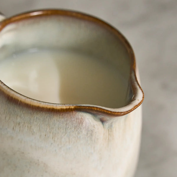 Cream ceramic milk jug with brown glazed rim on a marble tabletop