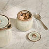 Cream ceramic sugar pot with brown glazed rim, filled with brown sugar cubes on a marble tabletop.