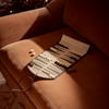 An open backgammon set with white and dark checkers laid out on a brown velvet armchair in warm, moody lighting. A few dice are placed nearby on the chair.