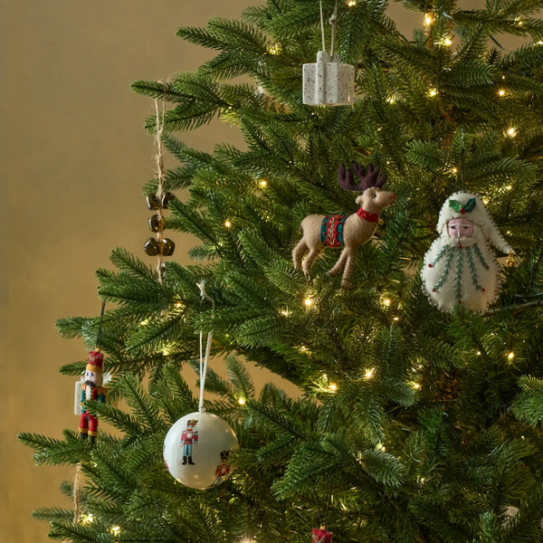 A close-up of a decorated Christmas tree with warm white lights, featuring handmade ornaments including a reindeer, a white bird figure, a round white ornament, and a nutcracker.