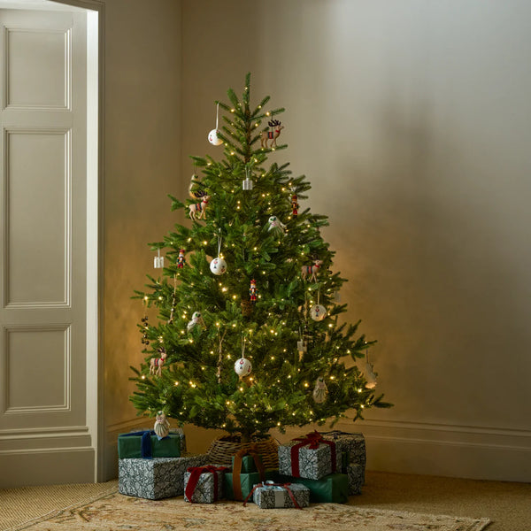 A decorated Christmas tree stands in a warmly lit room corner, with wrapped gift boxes underneath and a light-colored paneled door on the left.