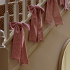 Pink and white vertically striped fabric ribbons tied in bows and draped over a cream-colored wooden staircase railing.
