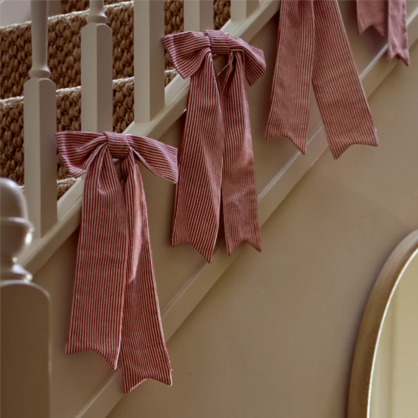 Pink and white vertically striped fabric ribbons tied in bows and draped over a cream-colored wooden staircase railing.