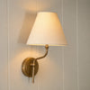 Regency wall light in brass with linen shade on cream wall, light on