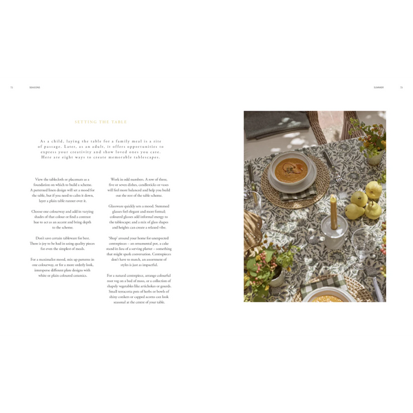 An open magazine or book spread showing interior design text on the left and a styled dining table scene on the right. The right panel shows a round table set with a white tablecloth, woven placemats, soup, candles, and green apples, with the caption 'SETTING THE TABLE.