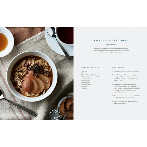 An open cookbook spread showing a styled breakfast scene on one page and a recipe for Chai Breakfast Bowl on the other. The left page includes a bowl of oatmeal with sliced pears, tea, star anise, and a spoon on a textured cloth.