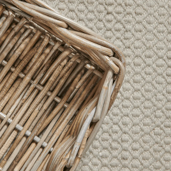 Close-up of a woven natural rattan or wicker basket corner with slatted sides, placed on a textured cream fabric background.