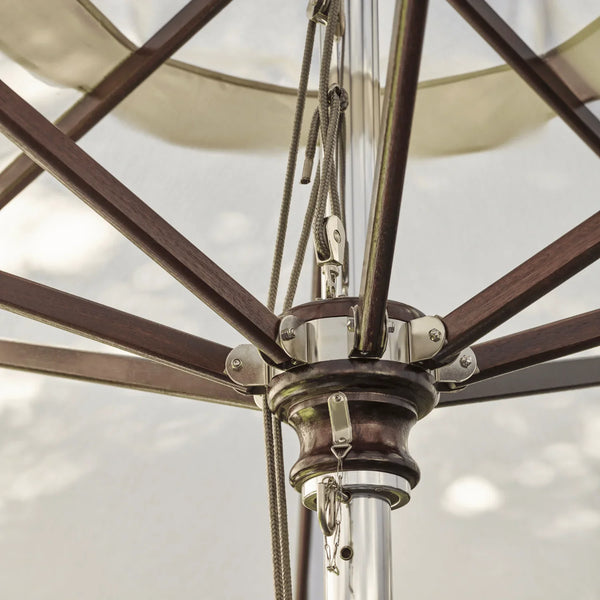 Close-up detail of an outdoor patio umbrella showing the central metal canopy attachment, dark brown wooden ribs, silver hardware, and part of the light-colored fabric canopy.
