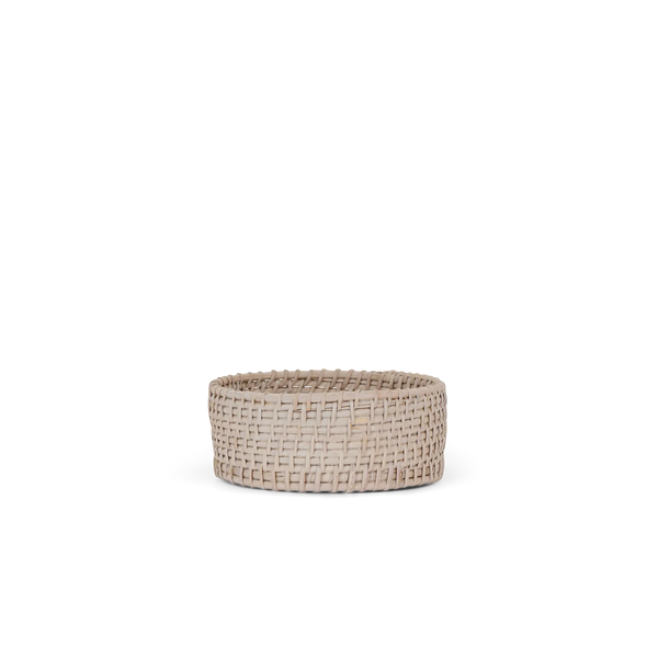 A small round woven basket made from natural light brown reed or straw fibers, photographed against a solid white background.