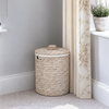 A round woven rattan storage basket with a lid, next to a patterned curtain and windowsill.