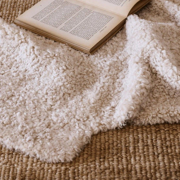 A close-up of a soft, fluffy cream sheepskin rug draped over a woven brown jute rug, with an open book placed on top.
