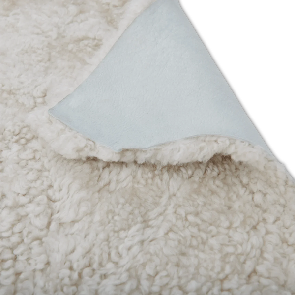 Close-up of a plush sherpa or faux-shearling fabric in warm off-white, with one corner folded back to reveal a pale blue underside.