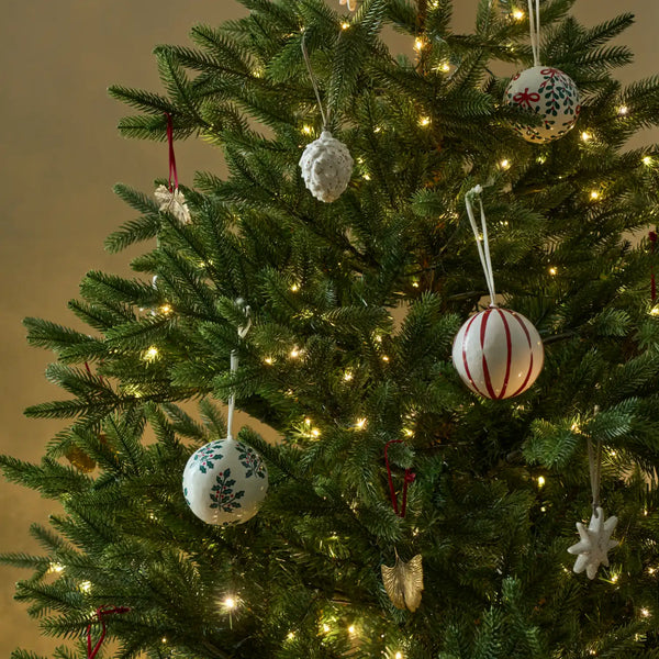 A close-up of a decorated Christmas tree with warm white string lights and several hanging ornaments, including white patterned baubles, a white textured ball, and a white snowflake ornament.