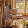 Wooden armchair with patterned cushions in a room with a large window and decorative elements.