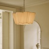 Pleated fabric pendant light with scalloped shade, hanging from a bronze chain in a hallway with an arched doorway.