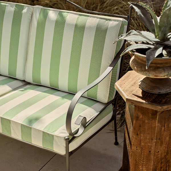Green and white striped outdoor sofa with a wooden side table and plant in the background