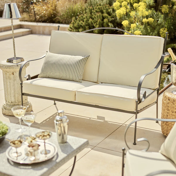 Beige outdoor sofa with cushions on a patio with a table and decorative items.