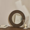 Round wooden mirror on a wall with a candle in a glass holder.