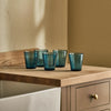 Six small blue textured glass tumbler s with a speckled finish, shown on a kitchen countertop with a neutral background.