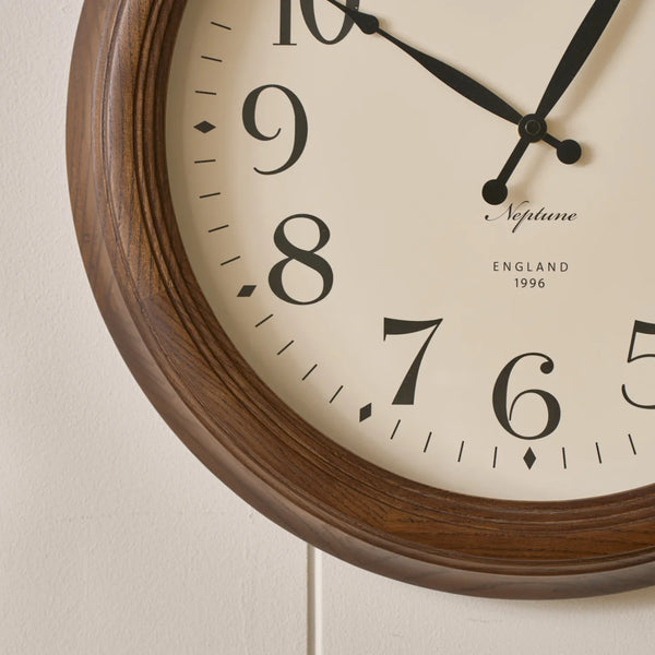 Close-up of a wall clock with a dark brown wood frame, cream-colored dial, black numerals, and black hands. The brand name 'Naptime' and 'ENGLAND 1996' are printed on the face, mounted on a light beige textured wall.