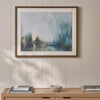A framed abstract landscape painting with soft blue, green, and gray tones, displayed on a cream paneled wall above a light wood console table with books and a small bowl.