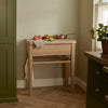 A natural finish Borough Oak Butchers Chopping Block placed in a kitchen setting, with a cloth and some fruits on top, showcasing its use as a kitchen prep surface.