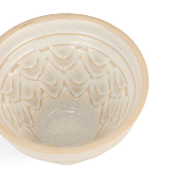 Close-up top-down view of a ceramic jelly mould bowl with a textured, embossed leaf or scale pattern inside, featuring a warm cream and light tan glaze on a white background.