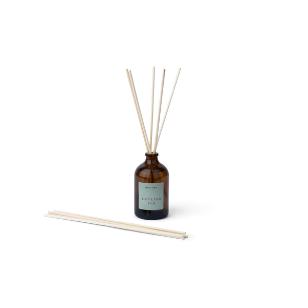 Amber glass reed diffuser bottle in English Fig fragrance with a pale green label, shown with five natural reed sticks standing upright and five reed sticks lying horizontally on a clean white background.