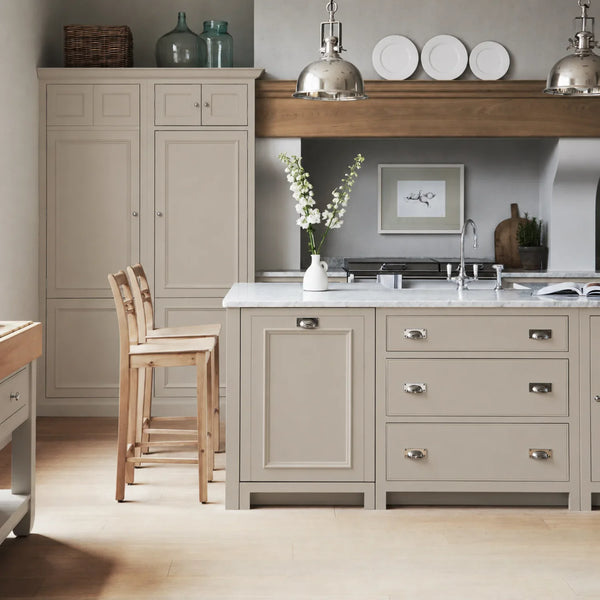 Chichester kitchen with cabinetry painted in Driftwood beige grey, featuring a central island and oak bar stools.