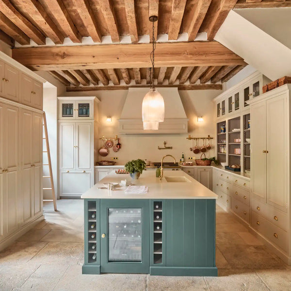 Traditional Chichester kitchen with driftwood neutral painted cabinetry, constable green island, hanging glass pendants, exposed timber beams and stone flooring.