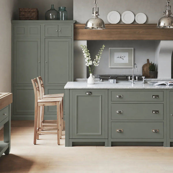 Chichester kitchen with cabinetry painted in Cactus green, featuring a central island and oak bar stools.